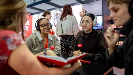 drei Frauen mit Kopfhörern, eine Frau mit geöffnetem Buch